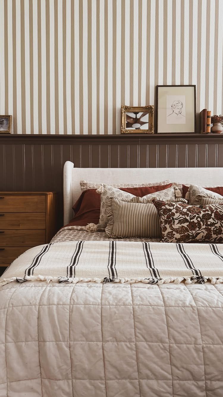 Dark brown beadboard wainscoting on a bedroom wall behind a bed with patterned pillows.