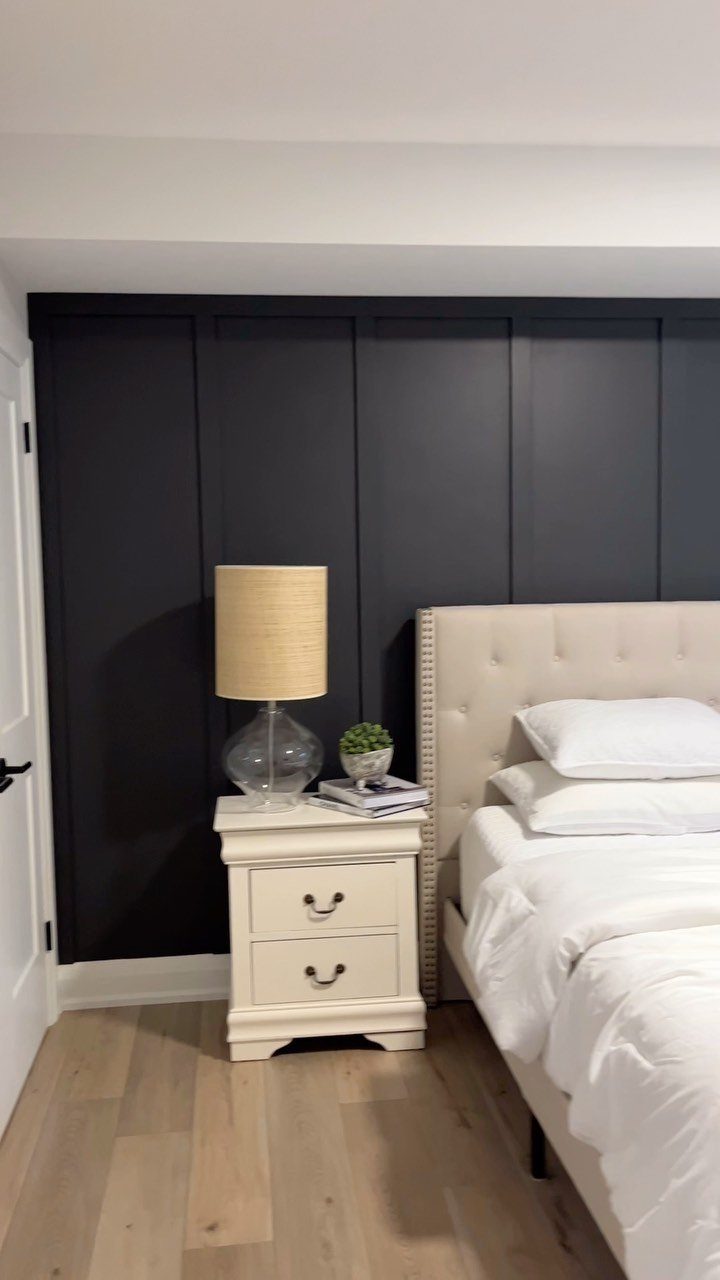Dark navy blue board-and-batten wall paneling behind a beige tufted bed and white nightstand.