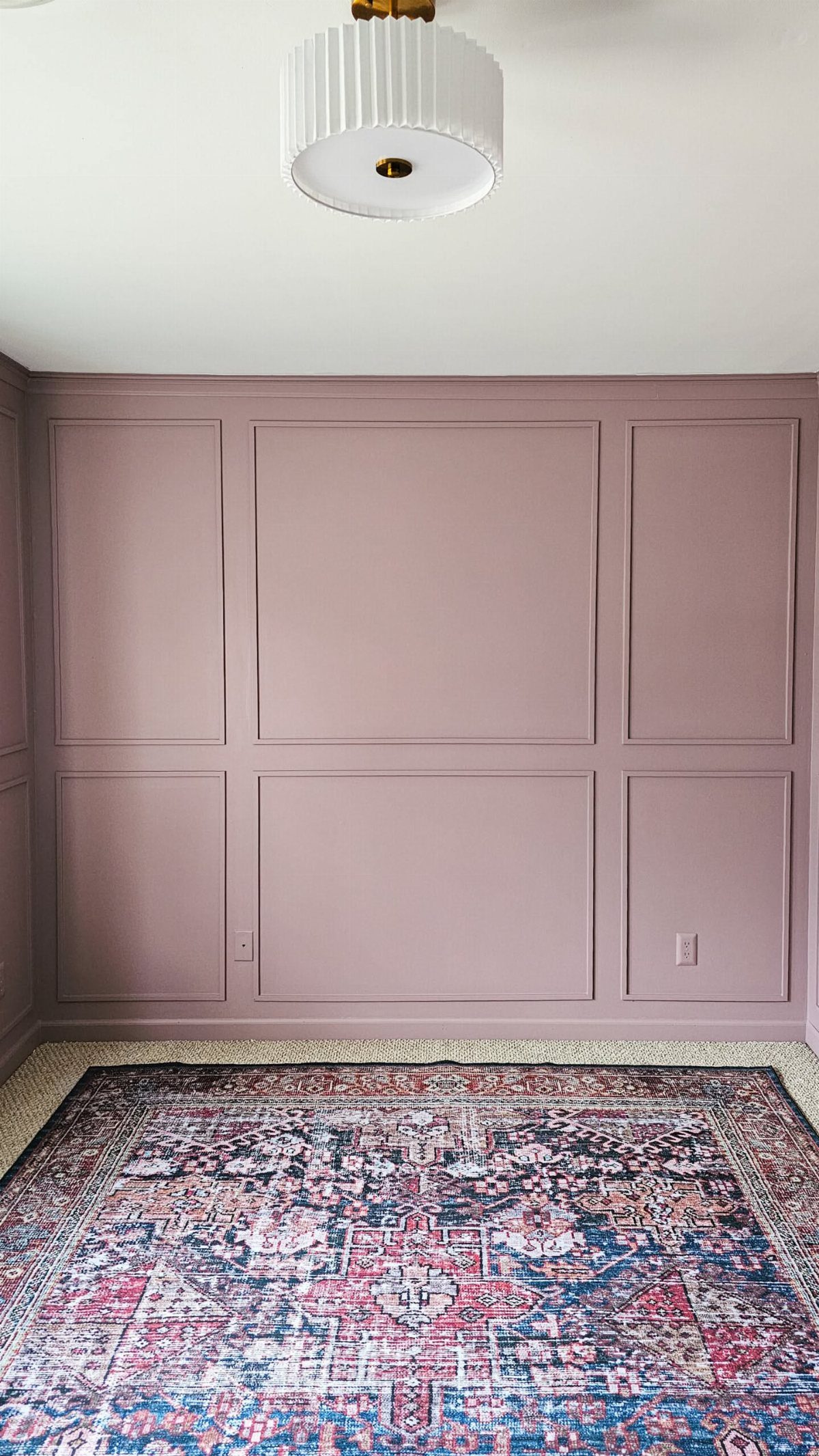 Dusty pink wall with geometric rectangular panel wainscoting and a patterned rug below.