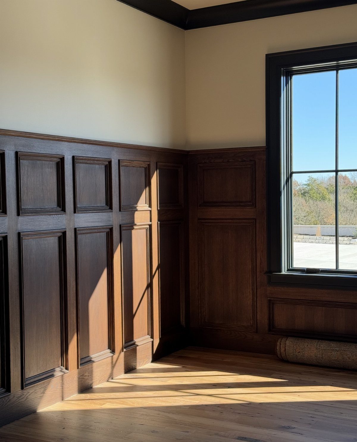 Dark wood raised panel wainscoting installed on the lower walls of a sunlit room.