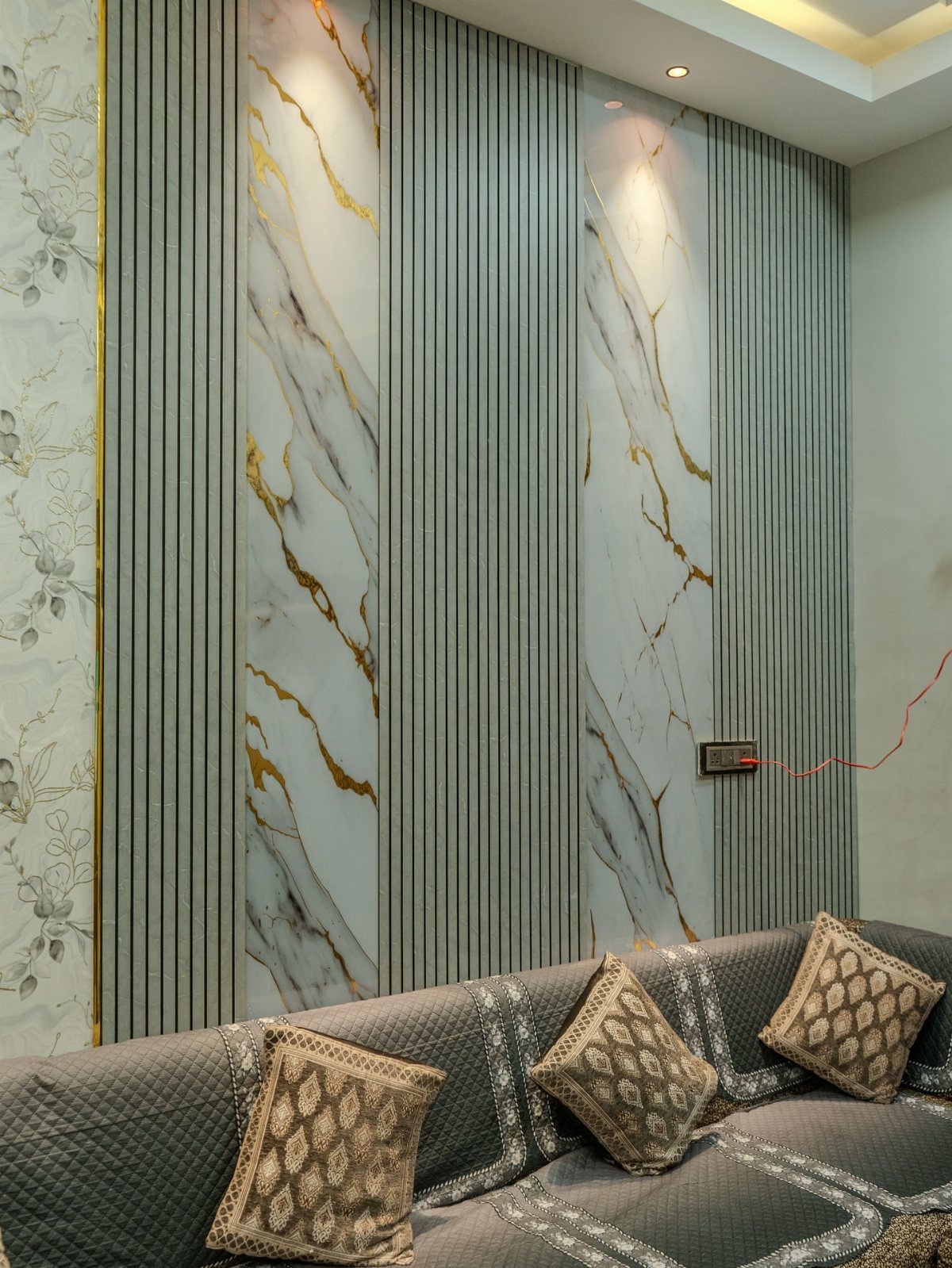 Grey fluted wall panels with marble-patterned sections and gold veining behind a grey sofa.