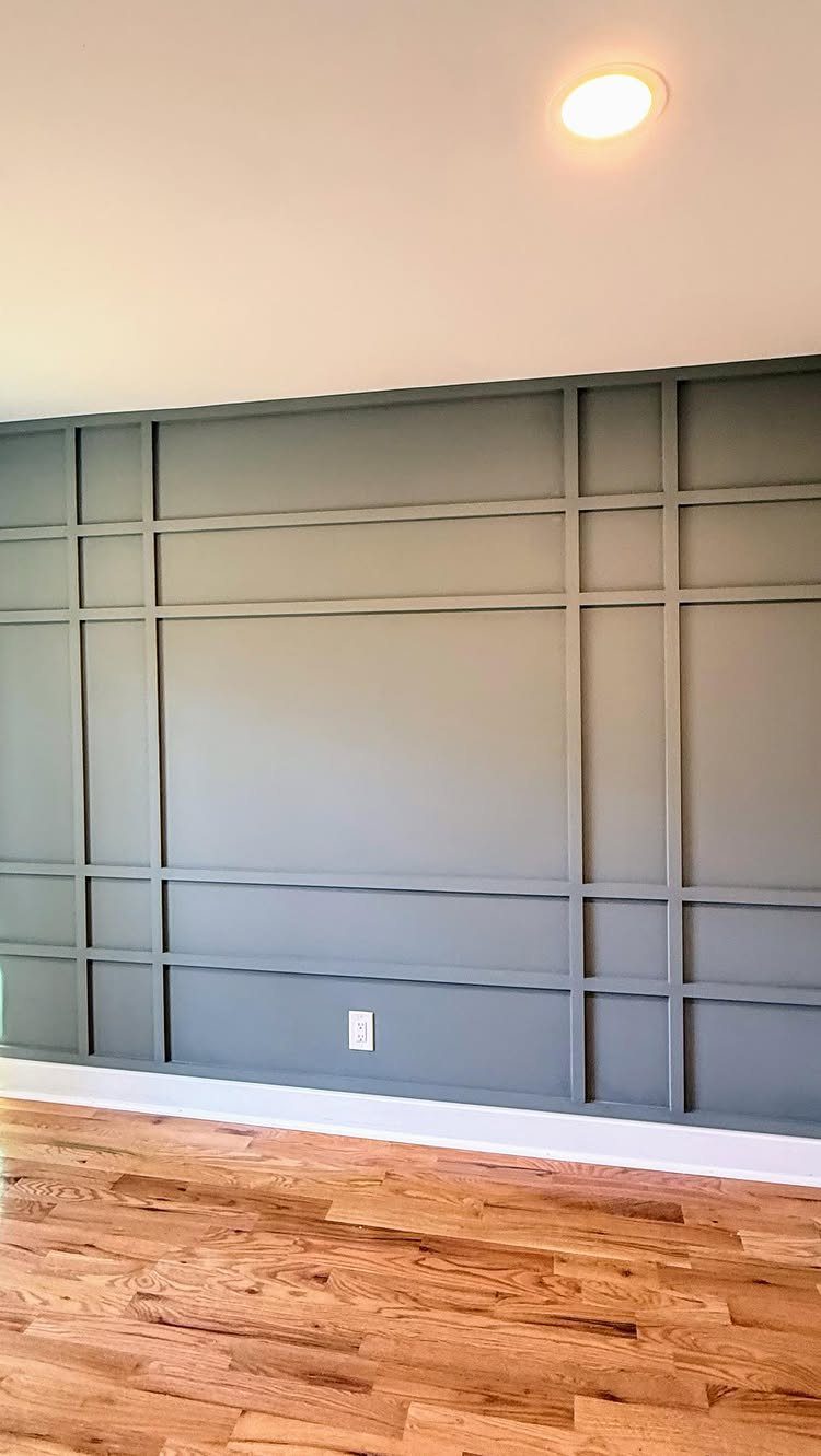 Grey wall with rectangular grid paneling above a light wood floor.