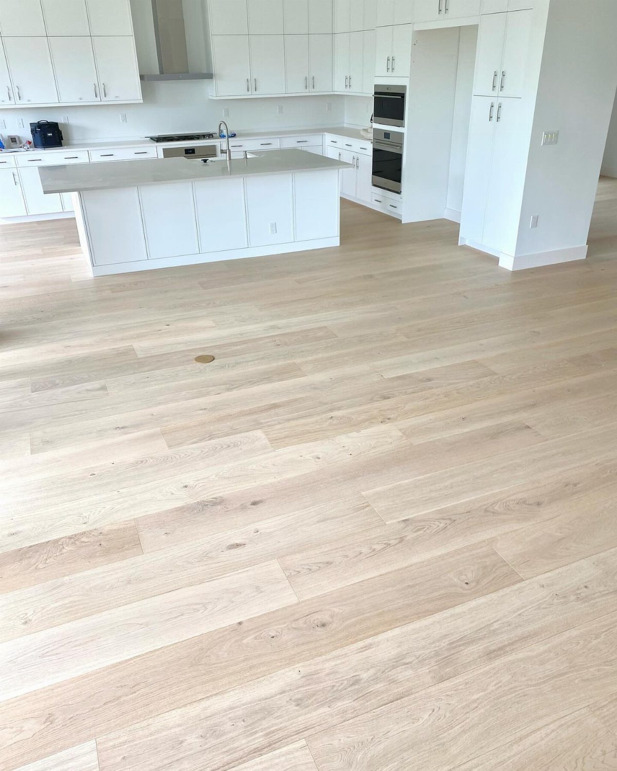 Light blonde wide plank hardwood floors in a modern white kitchen setting.