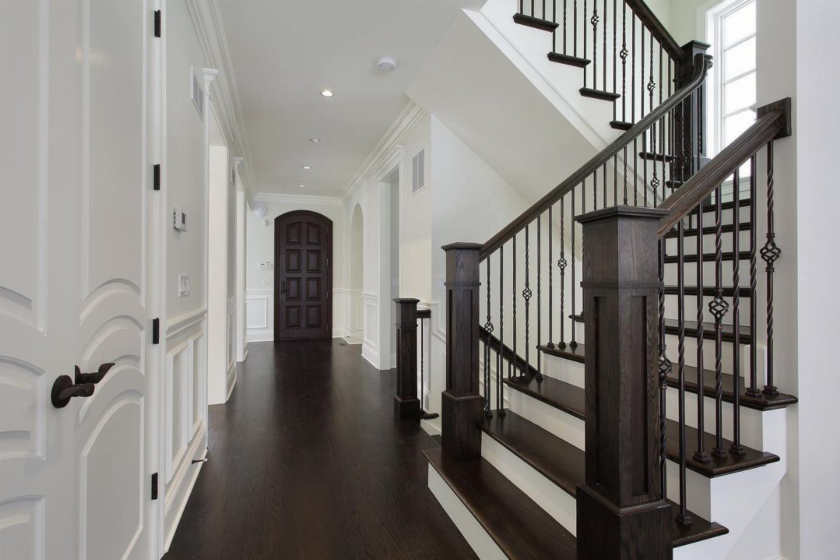 Dark espresso hardwood flooring in a bright hallway with white walls and a matching staircase.