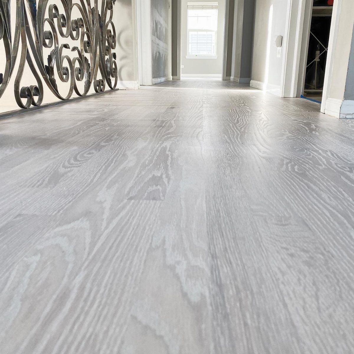 Light grey wood flooring with prominent grain patterns stretching through a bright, modern hallway.