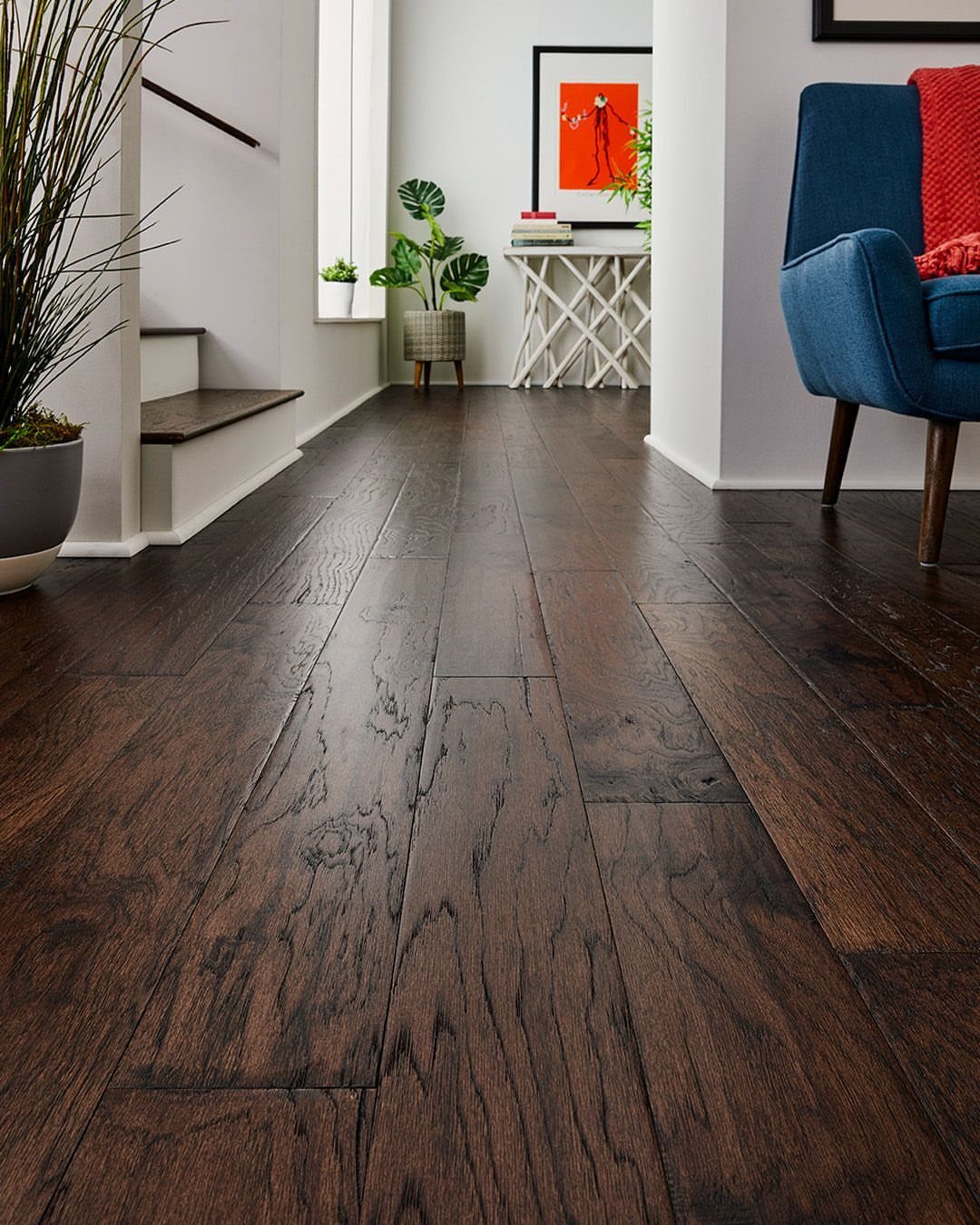 Dark brown wide plank hardwood flooring with a rustic hand-scraped texture in a bright room.