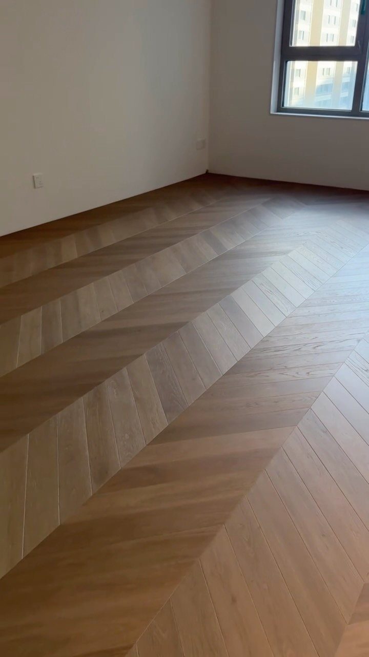 Chevron pattern wood flooring in a room with white walls and a window.