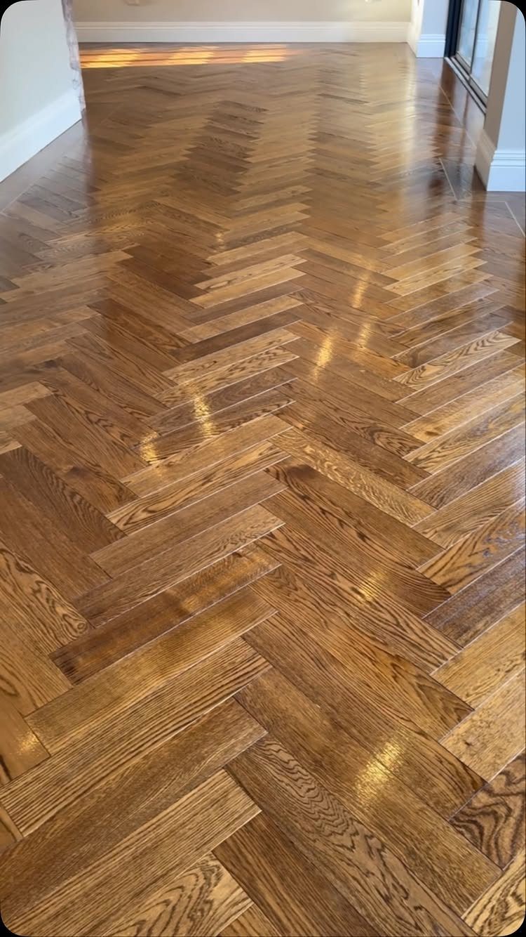 Herringbone pattern hardwood flooring with a glossy, warm brown finish reflecting natural light.
