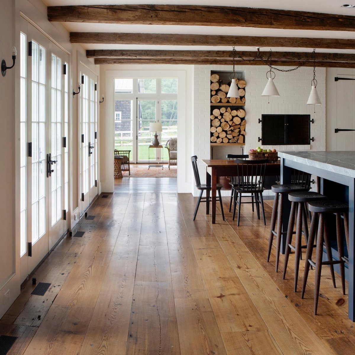 Wide planks of reclaimed wood flooring stretching through a bright, rustic kitchen with ceiling beams.