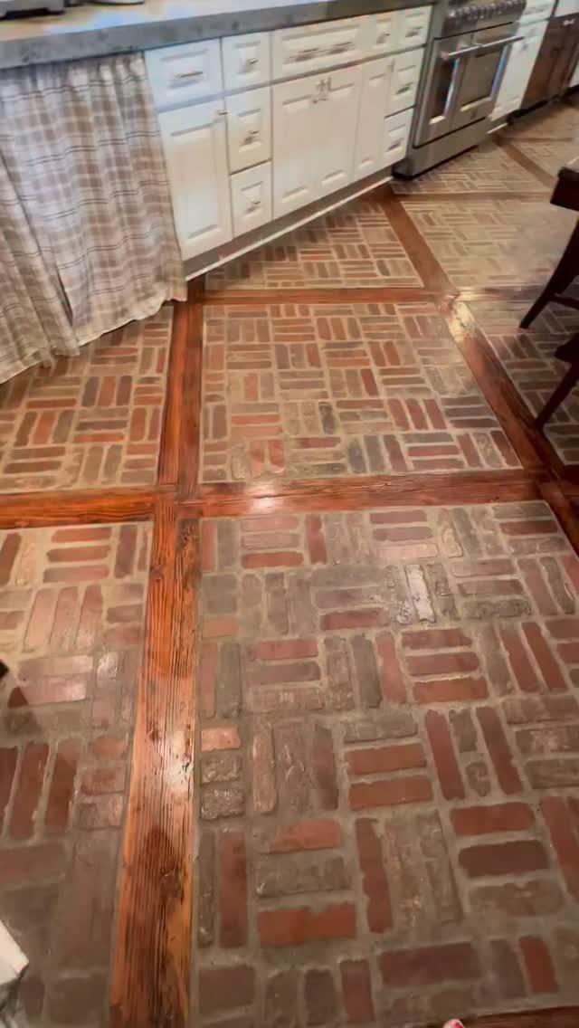 Brick flooring pattern framed by dark wood planks in a kitchen setting.